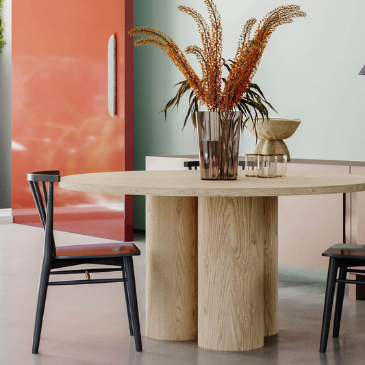 Modern dining room with round wood table, black chairs, coral wall, and dried pampas grass centerpiece
