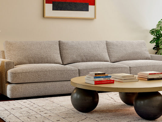 Modern gray sofa with round wood coffee table, abstract art, patterned rug, and stacked books in living room