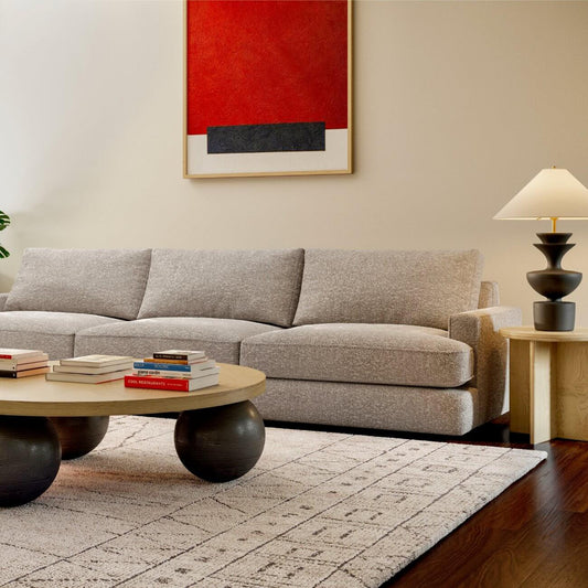 Modern living room with gray sectional sofa, geometric coffee table, red abstract art, patterned rug, and table lamp