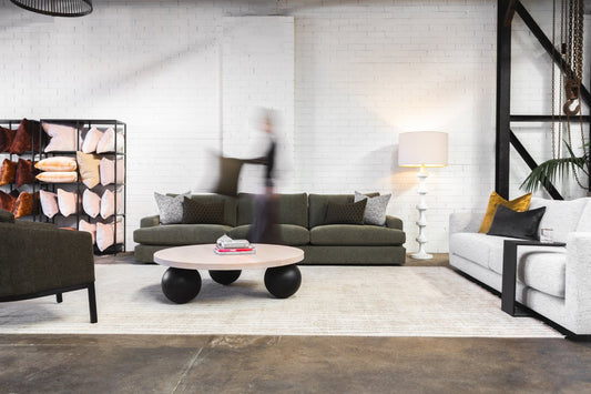Modern loft living room with olive sofa, round pink coffee table on black spheres, white brick walls, and pillow display