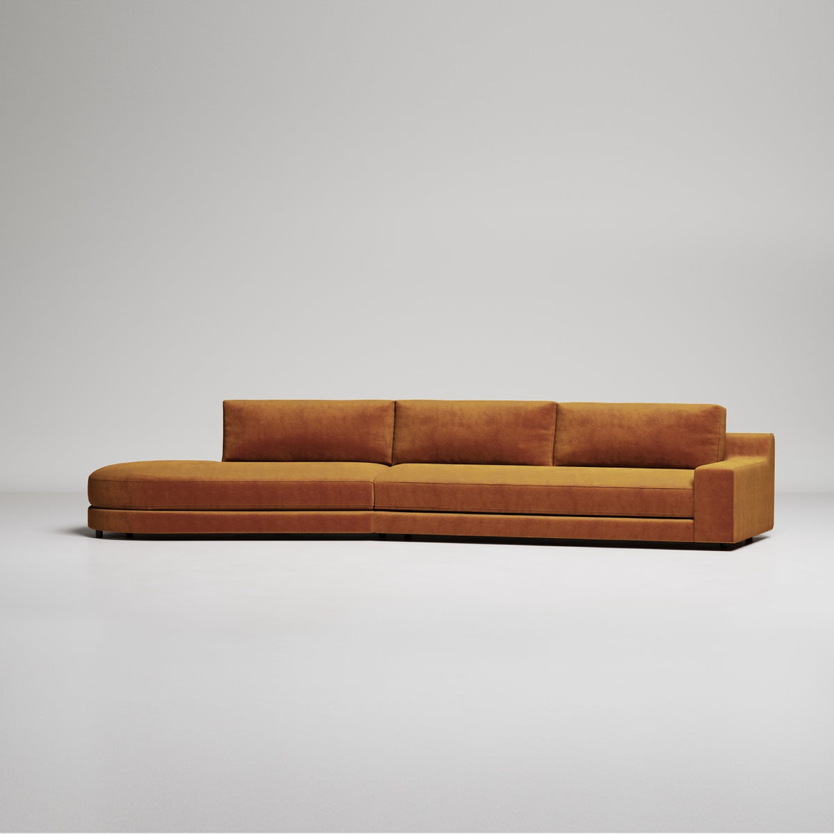Modern elongated sectional sofa in rich cognac velvet with clean lines and minimalist design against gray background
