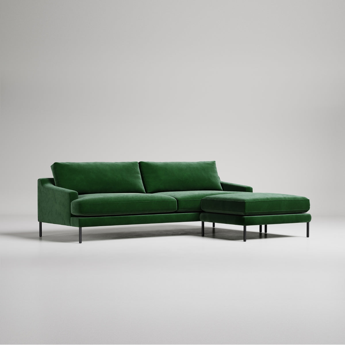 Modern emerald green velvet sectional sofa with ottoman on black metal legs, against light gray backdrop
