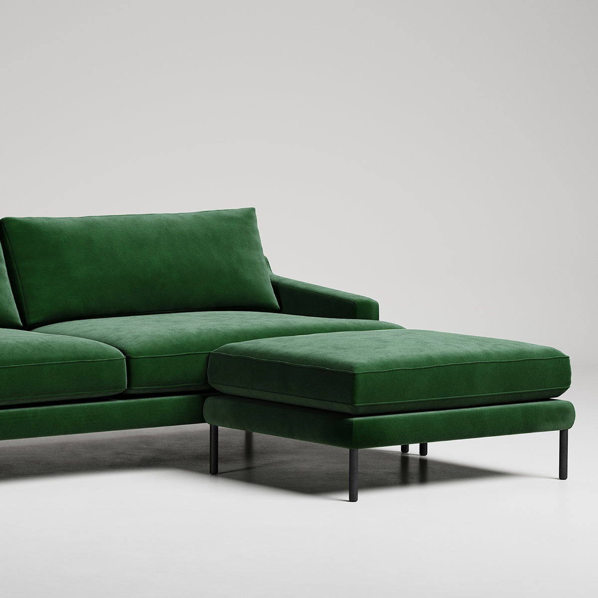 Modern green velvet sectional sofa with chaise ottoman on black metal legs against white background

