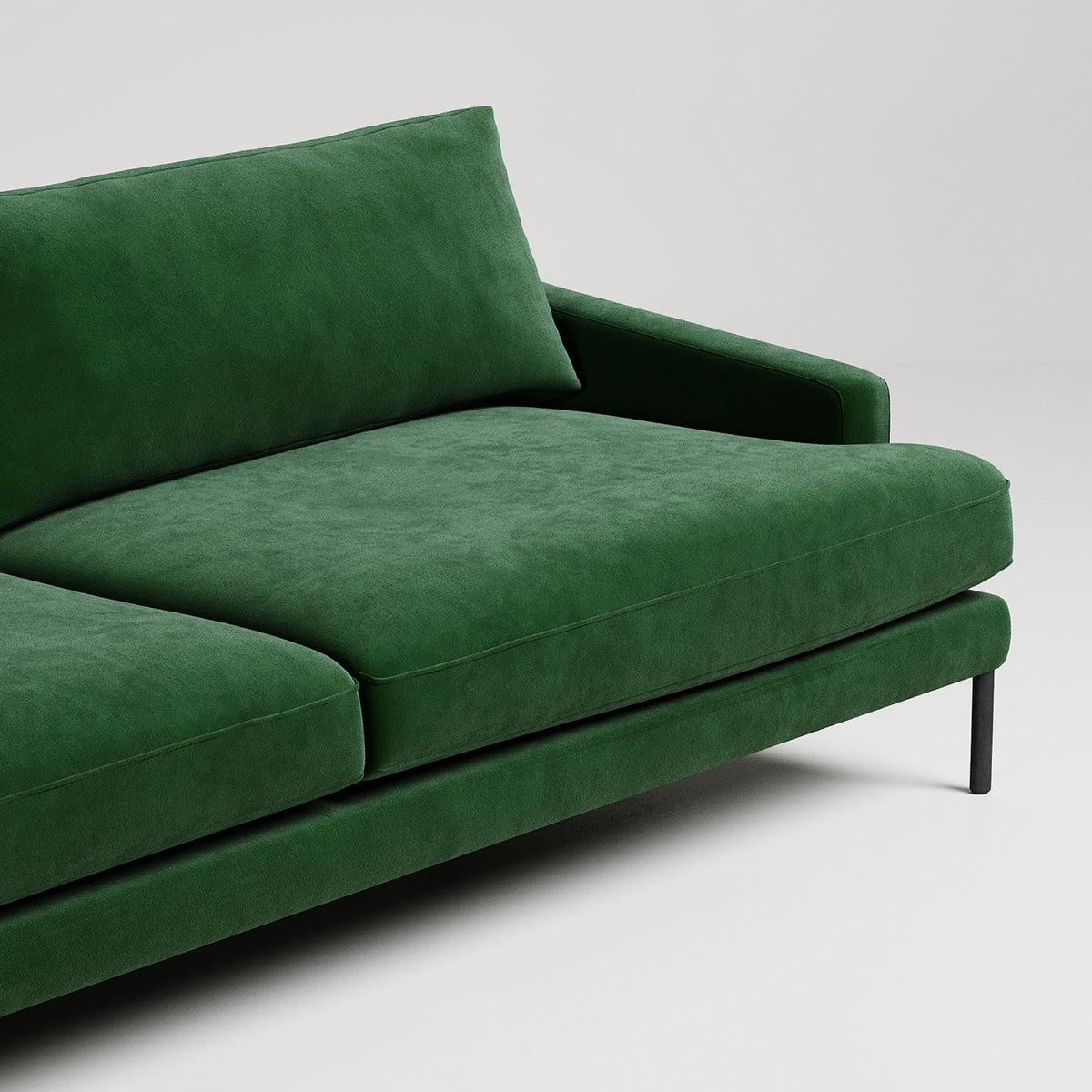 Modern emerald green velvet sofa with black metal legs on white background, minimalist design detail shot

