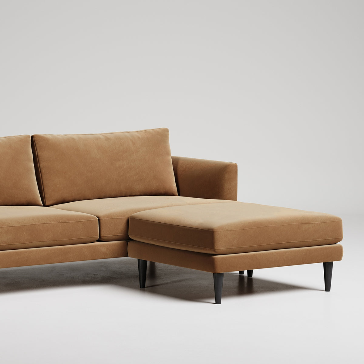 Modern tan leather sectional sofa with chaise lounge on black legs against white background
