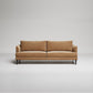 Modern tan leather sofa with slim black legs against neutral gray background, minimalist studio shot
