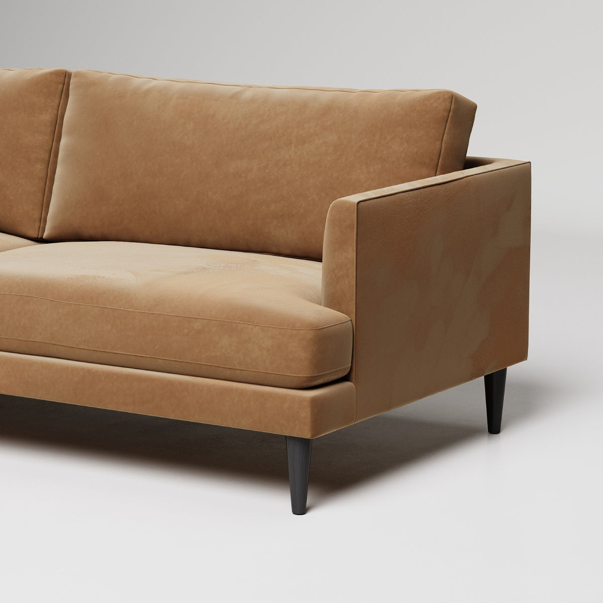 Modern tan leather sofa with clean lines and black tapered legs shown against white backdrop, detail view
