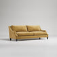 Modern gold velvet sofa with curved arms, black legs and plush cushions against light gray background
