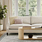 Modern living room with beige sofa, wood coffee table, patterned rug, large windows and indoor plant
