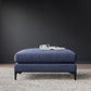 Blue upholstered ottoman with metal legs on gray carpet, open magazine on top, modern minimalist style

