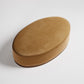 Oval-shaped velvet ottoman in camel brown with wooden base, photographed against white background
