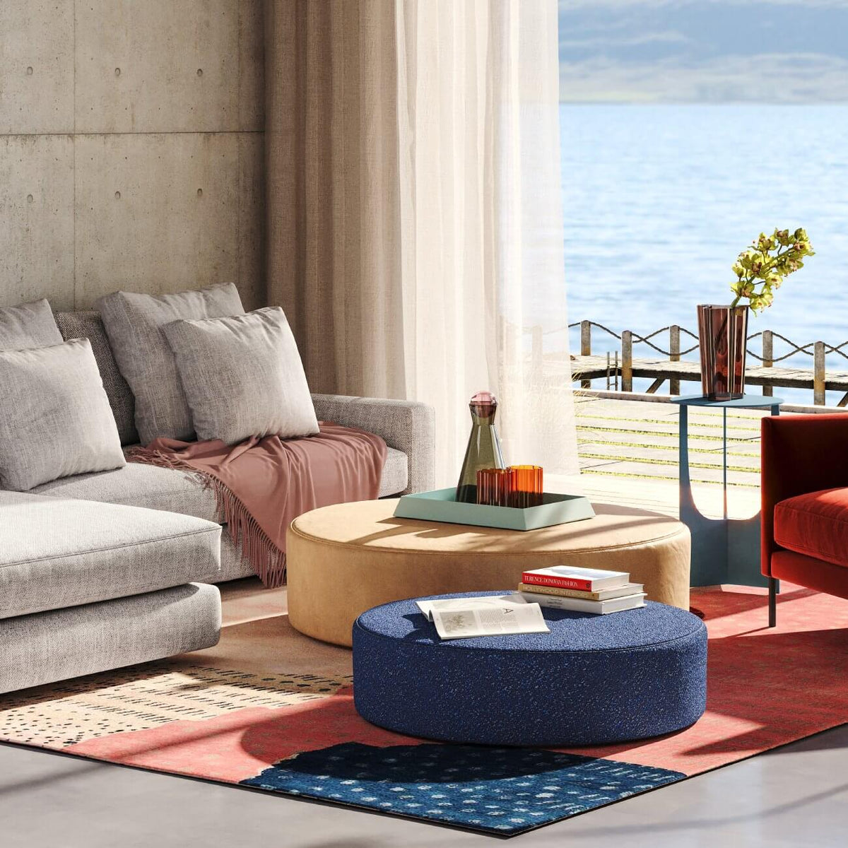 Modern coastal living room with gray sofa, round ottomans, ocean view, and coral accent rug
