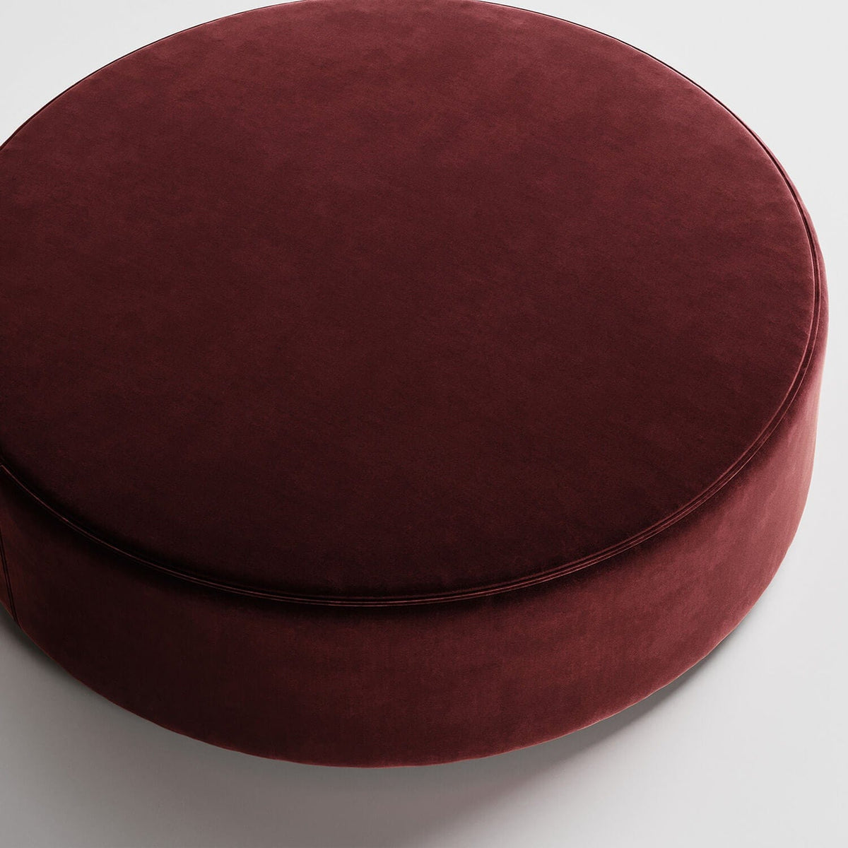 Round burgundy velvet ottoman or pouf against white background, viewed from above
