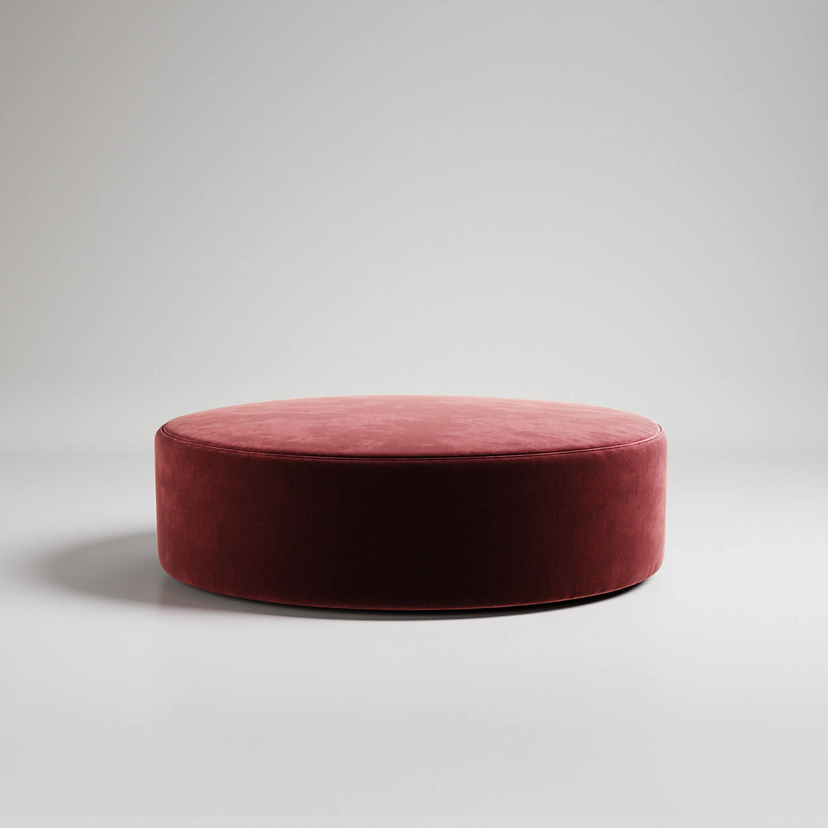 Large round burgundy velvet ottoman or footstool on white background, modern minimalist style
