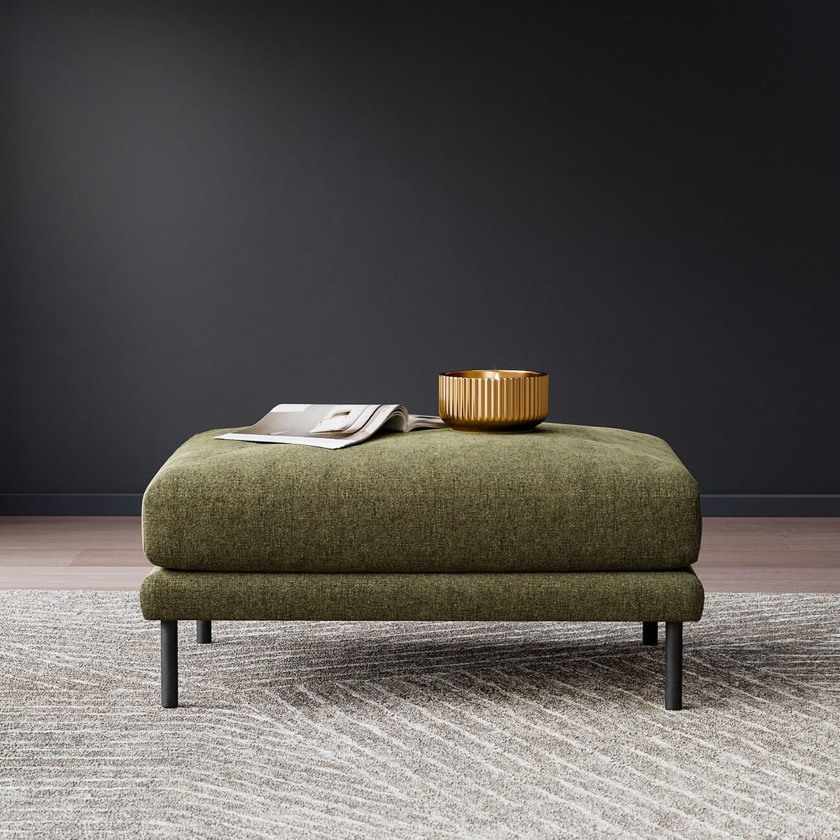 Modern olive green ottoman with black legs on gray rug, styled with gold bowl and magazine on top
