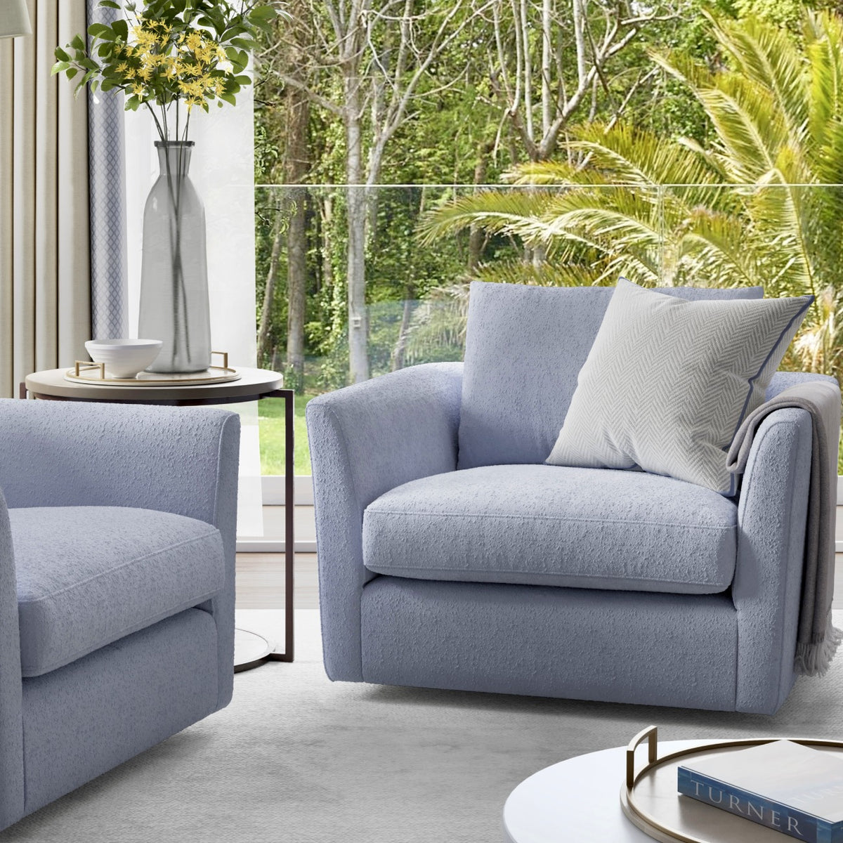 Modern gray swivel armchairs with throw pillows, side table with vase, tropical garden view through window
