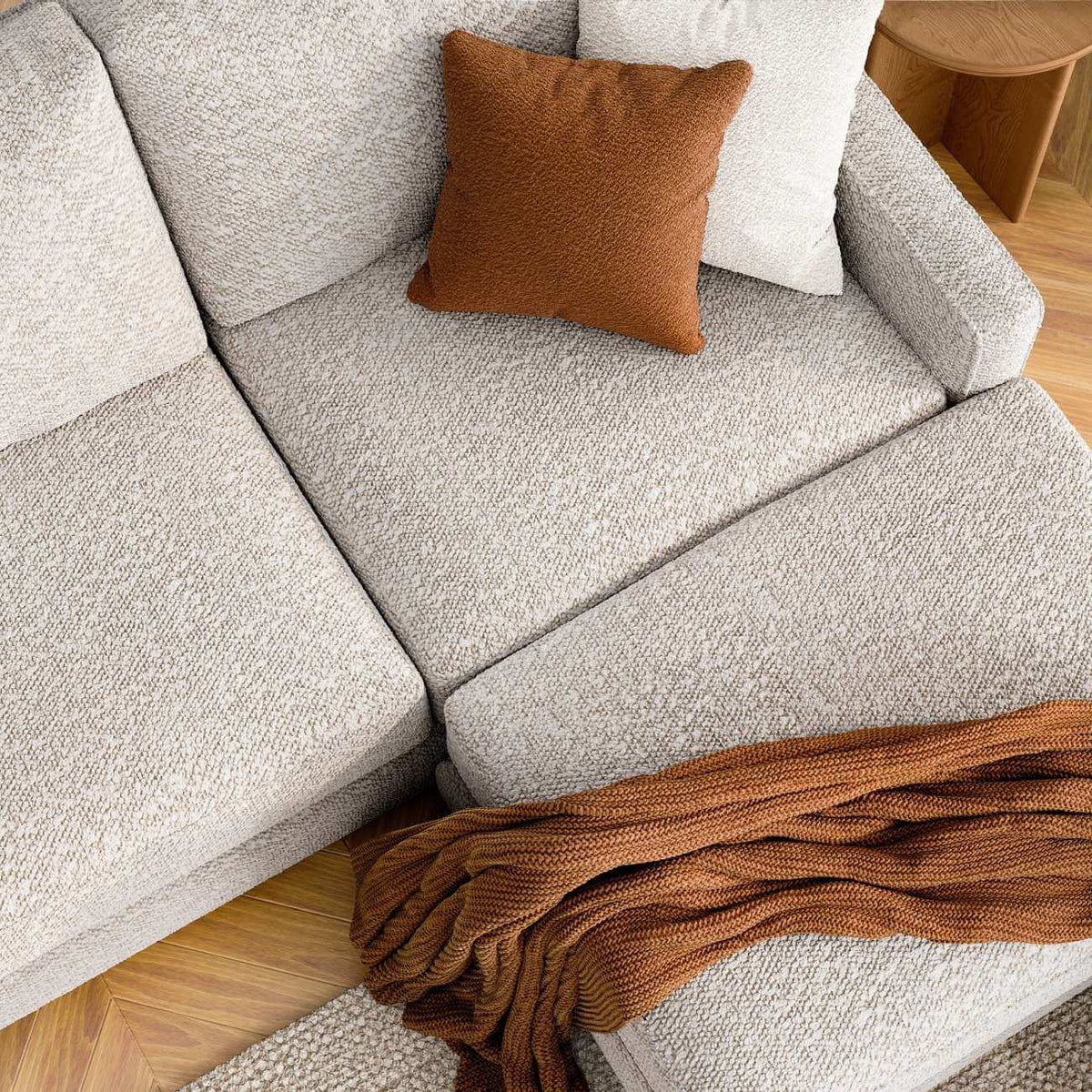 Light gray modern sofa with brown cushion and knit throw blanket on wood floor, cozy home decor styling
